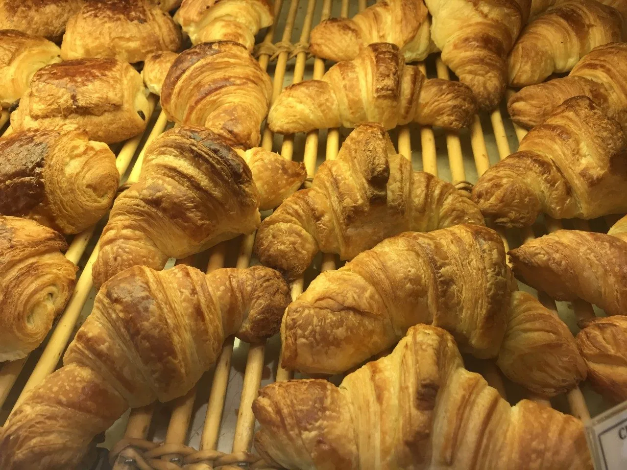 Croissant e pain au chocolat dorati allineati su un ripiano di vimini in una boulangerie