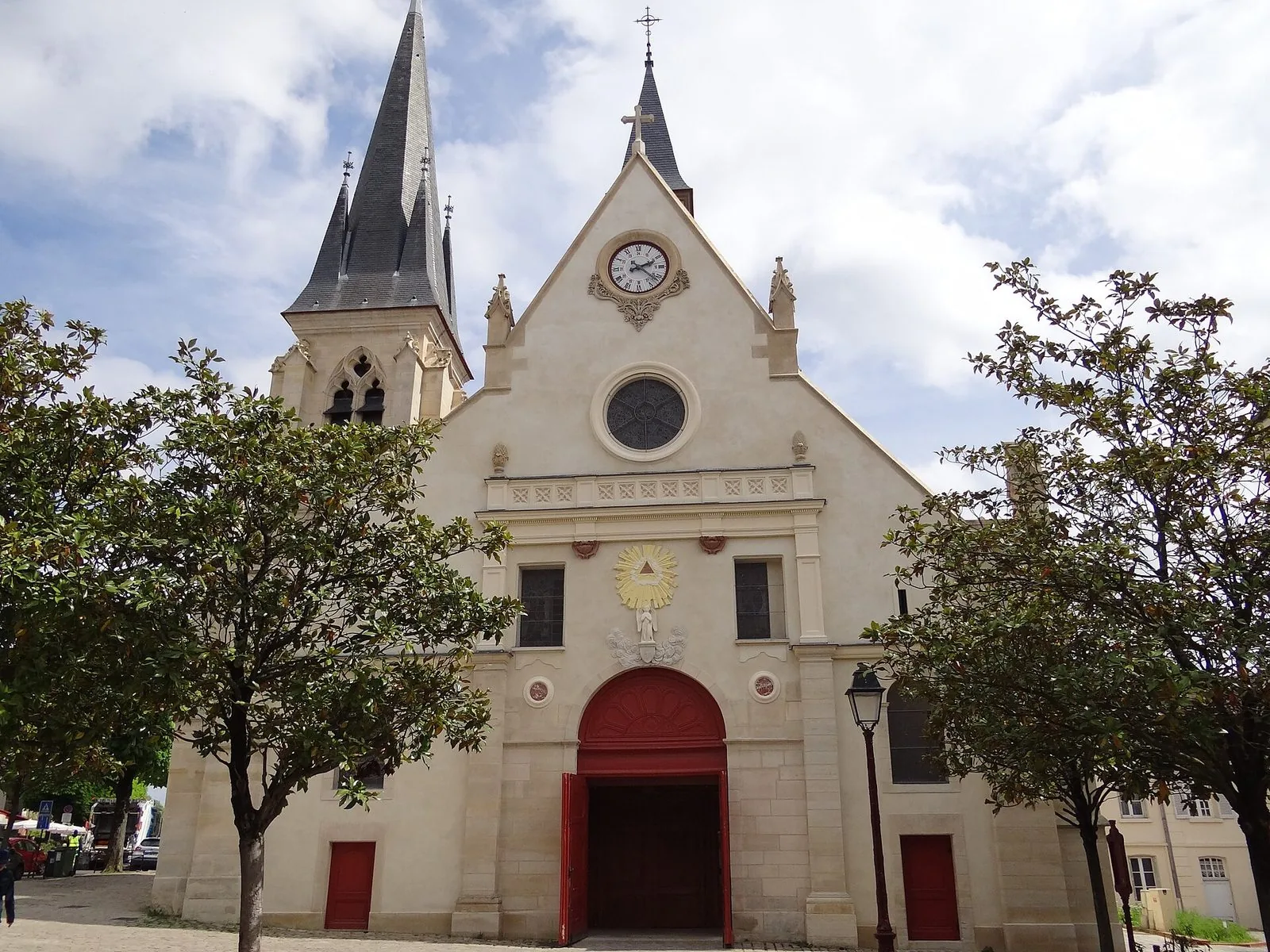 Facciata della chiesa Saint-Jean-Baptiste di Sceaux con il campanile a guglia, il rosone e il portale rosso tra gli alberi