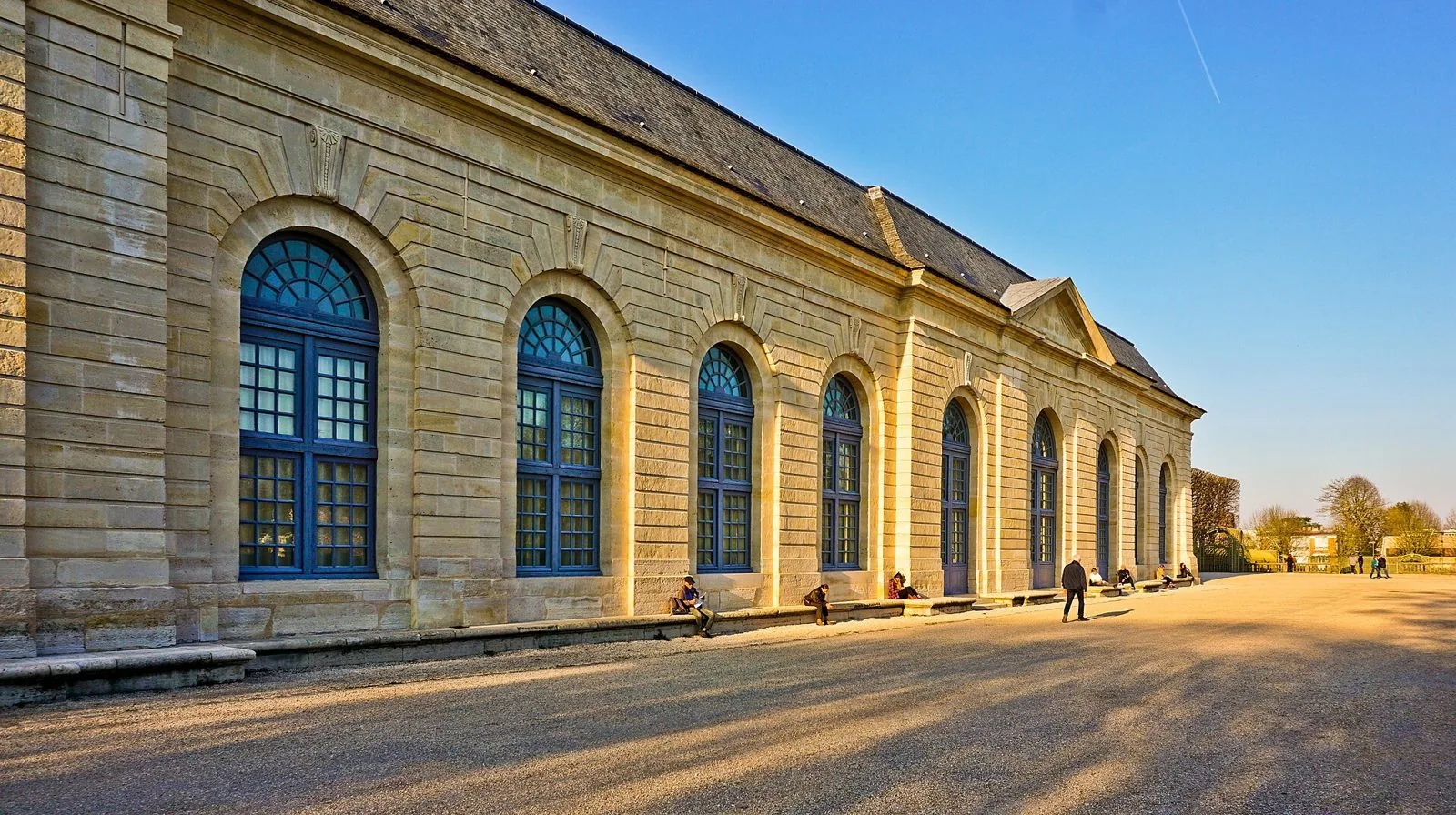 La lunga facciata in pietra dell'Orangerie del Domaine de Sceaux con le grandi finestre ad arco illuminate dal sole del pomeriggio