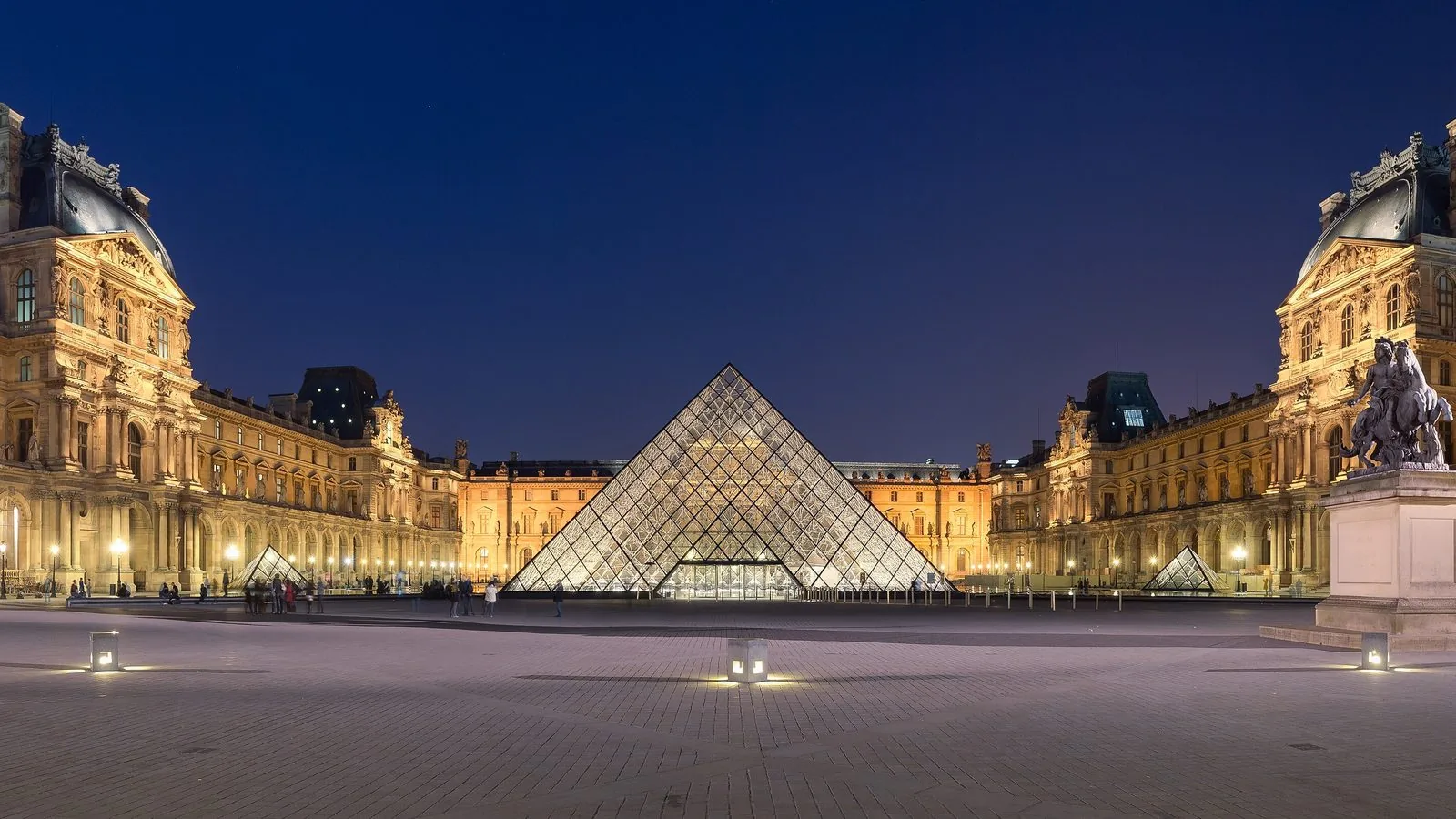 La Piramide del Louvre illuminata di sera al centro della Cour Napoléon, tra le ali del palazzo
